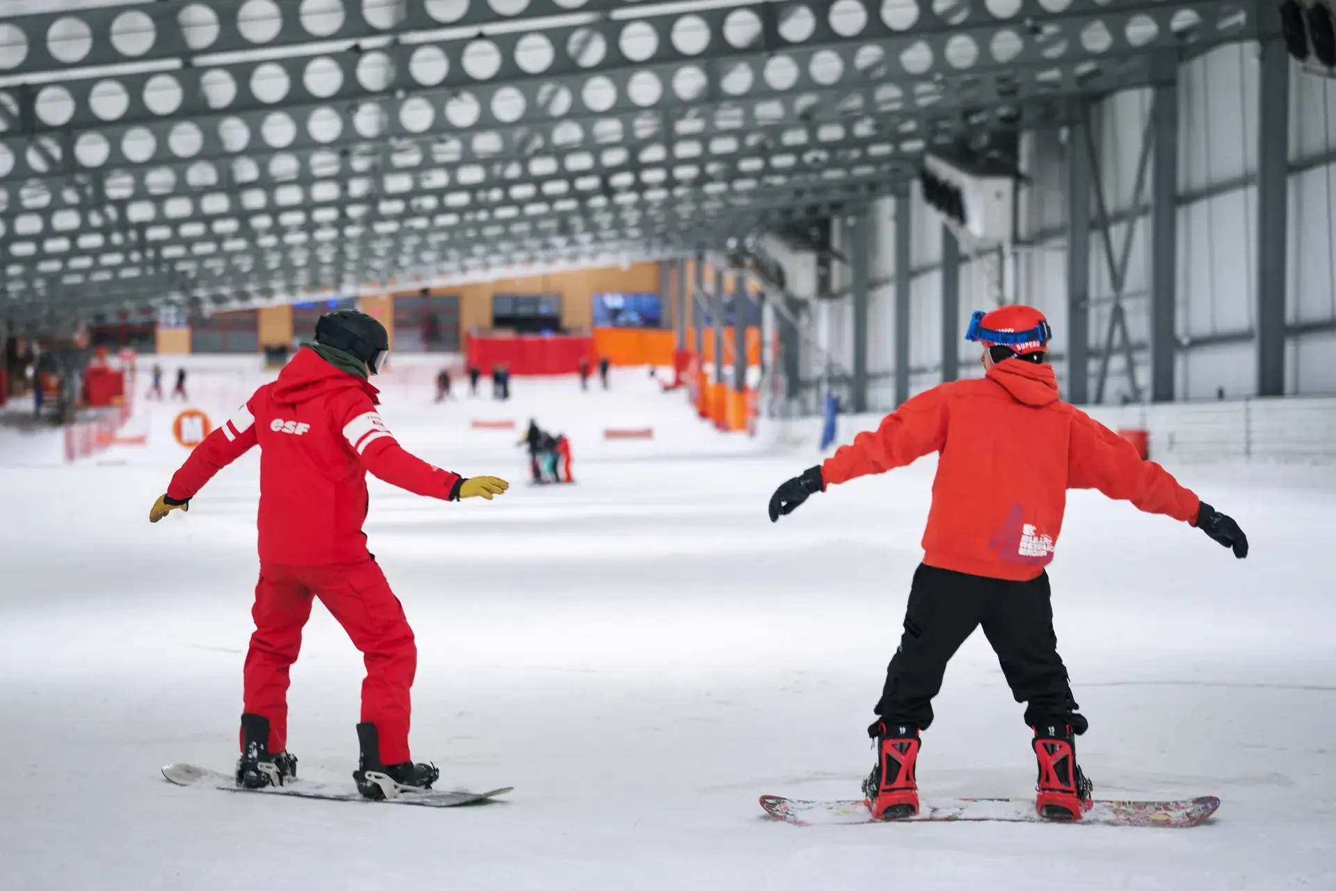 Moniteur ESF et élève descendant la piste indoor en snowboard
